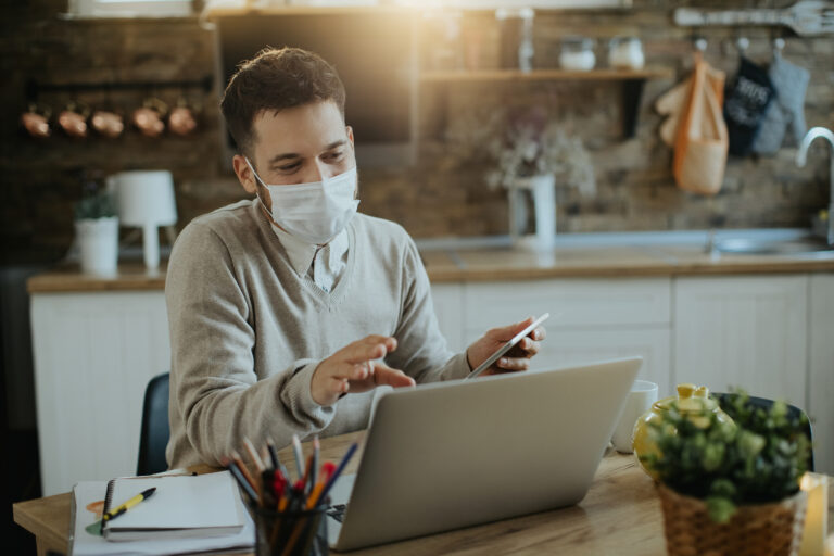Male entrepreneur with face mask having video call over laptop w